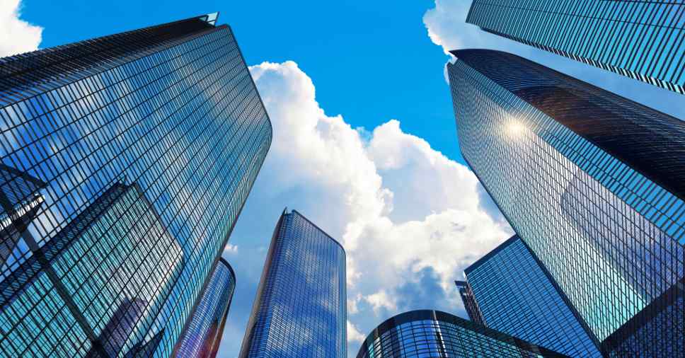 Vista inferior de prédios comerciais modernos sob céu azul indica que SST é obrigatório.