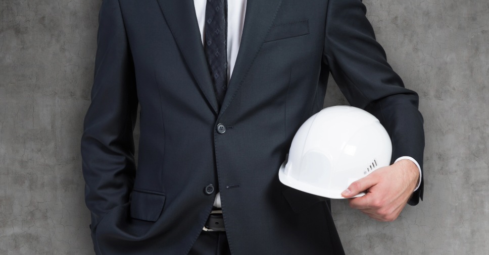 Homem de terno escuro e gravata segurando capacete branco para aprender como fazer PGR simples.